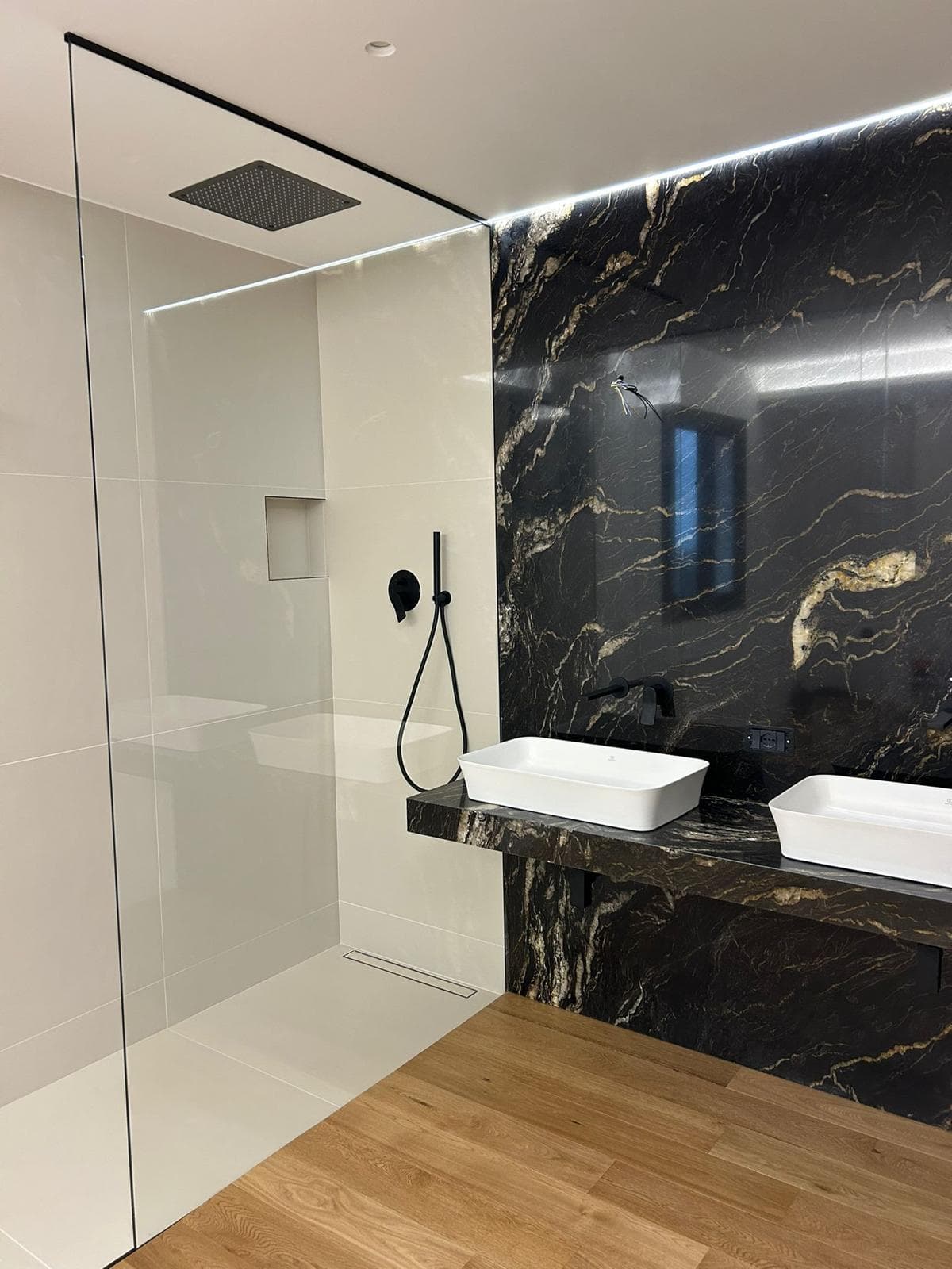 Bagno con parete in marmo nero e oro e doppio lavabo